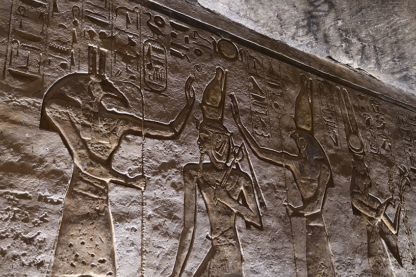 40 MAK_6557.jpg - Ramesse II riceve la benedizione e l'incoronazione dalle divinità. Le sue dimensioni, pari a quelle degli dei, indicano la sua natura divina e il suo status di Dio in terra. Horus (destra) rappresenta il cielo e l'ordine; Seth (sinistra) rappresenta il deserto e il caos. La presenza simultanea di Horus e Seth, acerrimi rivali nel mito, comunica che le forze opposte del cosmo sono ora riconciliate sotto il governo di Ramesse II, garantendo un'era di ordine e pace per l'Egitto.